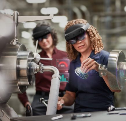 工作機械の前で、二人の女性がHoloLens 2 を装着しており、ひとりがホログラムを操作している。