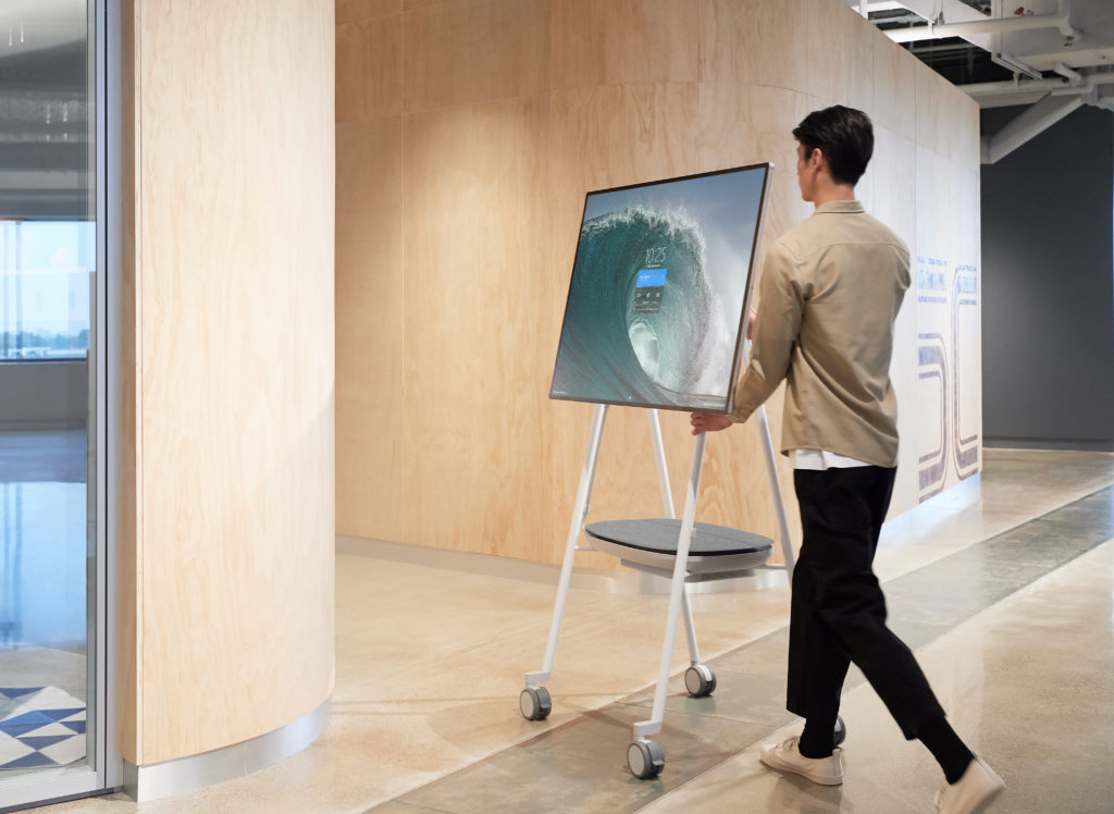 Man wheels a Surface Hub 2S into a meeting room