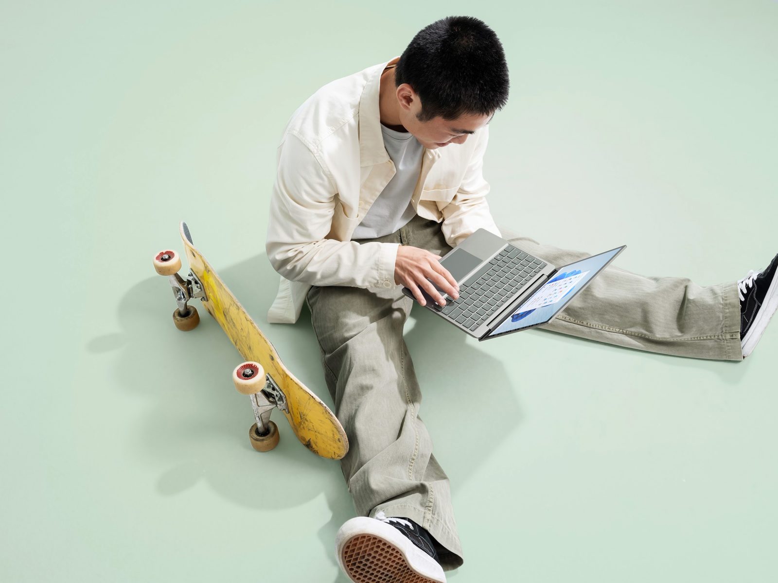 a person looks at laptop device with a skateboard next to him