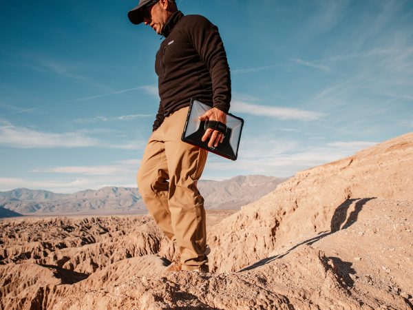 Man walking through a desert with a tablet device connected to his left hand with a strap